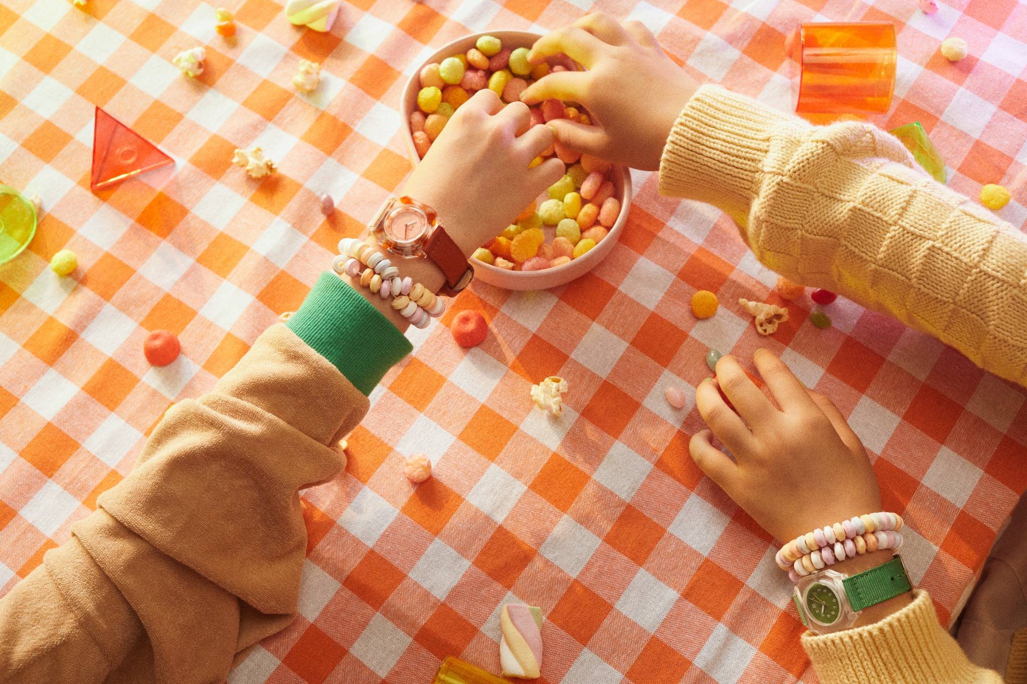Children wearing Mini Kyomo kids watches while reaching for colorful snacks on an orange checkered tablecloth Shopiva, UAE, Dubai