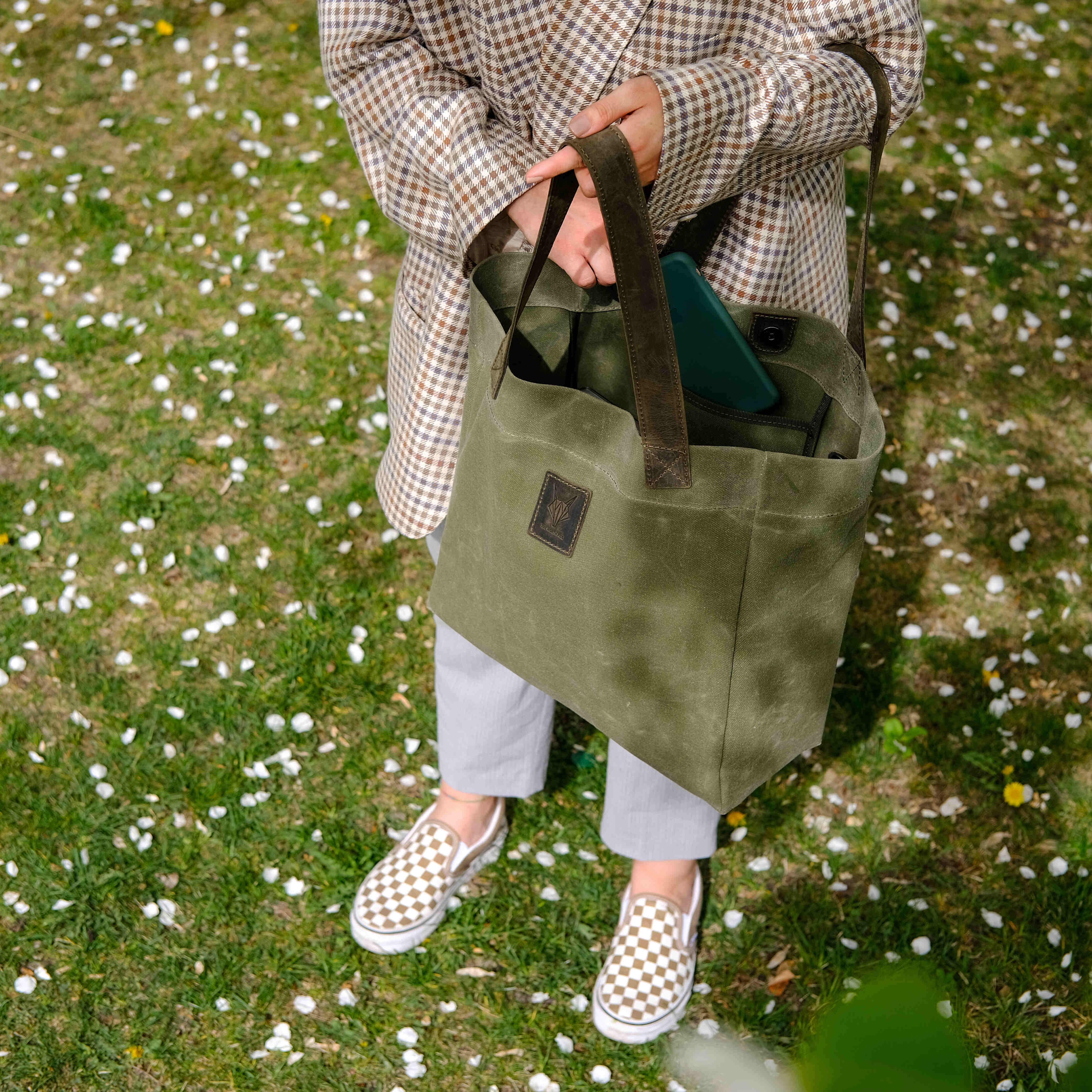 Lifestyle shot of a person holding an olive-green canvas tote bag outdoors on a grassy field