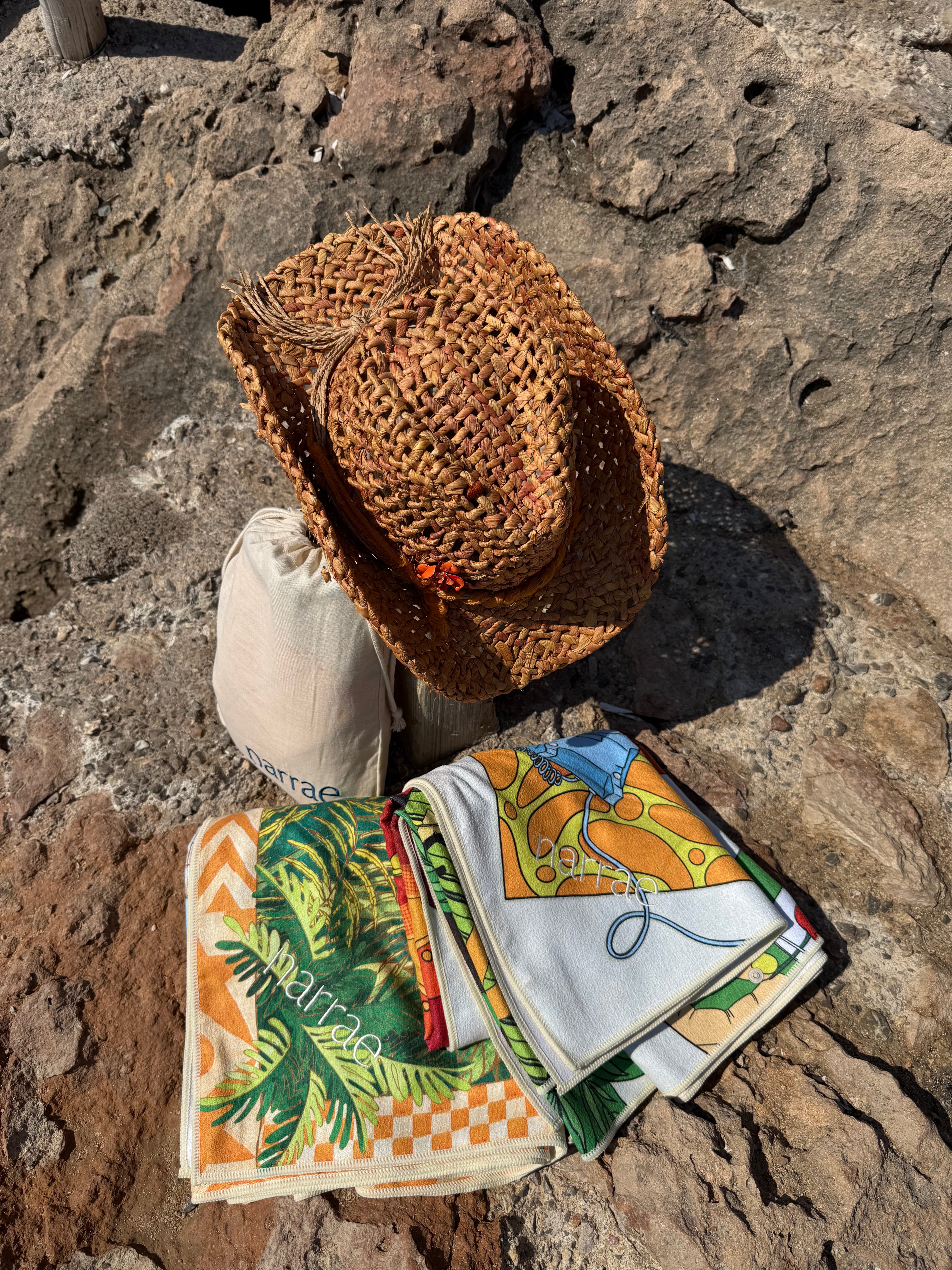 Colorful Narrae beach towels folded on rocks beside a straw hat in a sunny outdoor setting